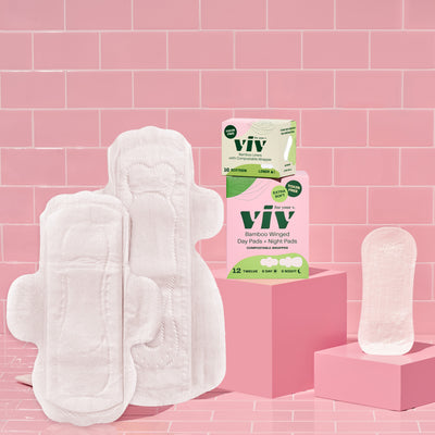 Combo Box Viv Day Pads, Night Pads, and Eco-Friendly, Toxin-Free Liners. A Winged Day Pad sits next to a Double-Winged Night Pad and an Extra Soft Liner, on a pink Tile Backdrop next to a box of Combo Day and Night Pads and a box of Viv Bamboo Liners