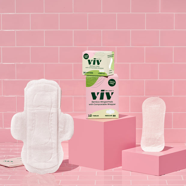 Viv Combo Box: Day Pads and Liners. Viv Eco-Friendly Winged Day Pad and Bamboo Biodegradable Liner sit on a pink tile background next to boxes of Viv Pads and Liners