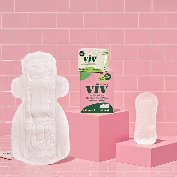 Viv Combo Box Double-Winged Night Pads and Bamboo Toxin-Free Liners. Ultra absorbent Viv night pad and an extra soft Viv Liner sit on a pink tile background next to a box of Viv Night pads and a box of Viv Bamboo Liners