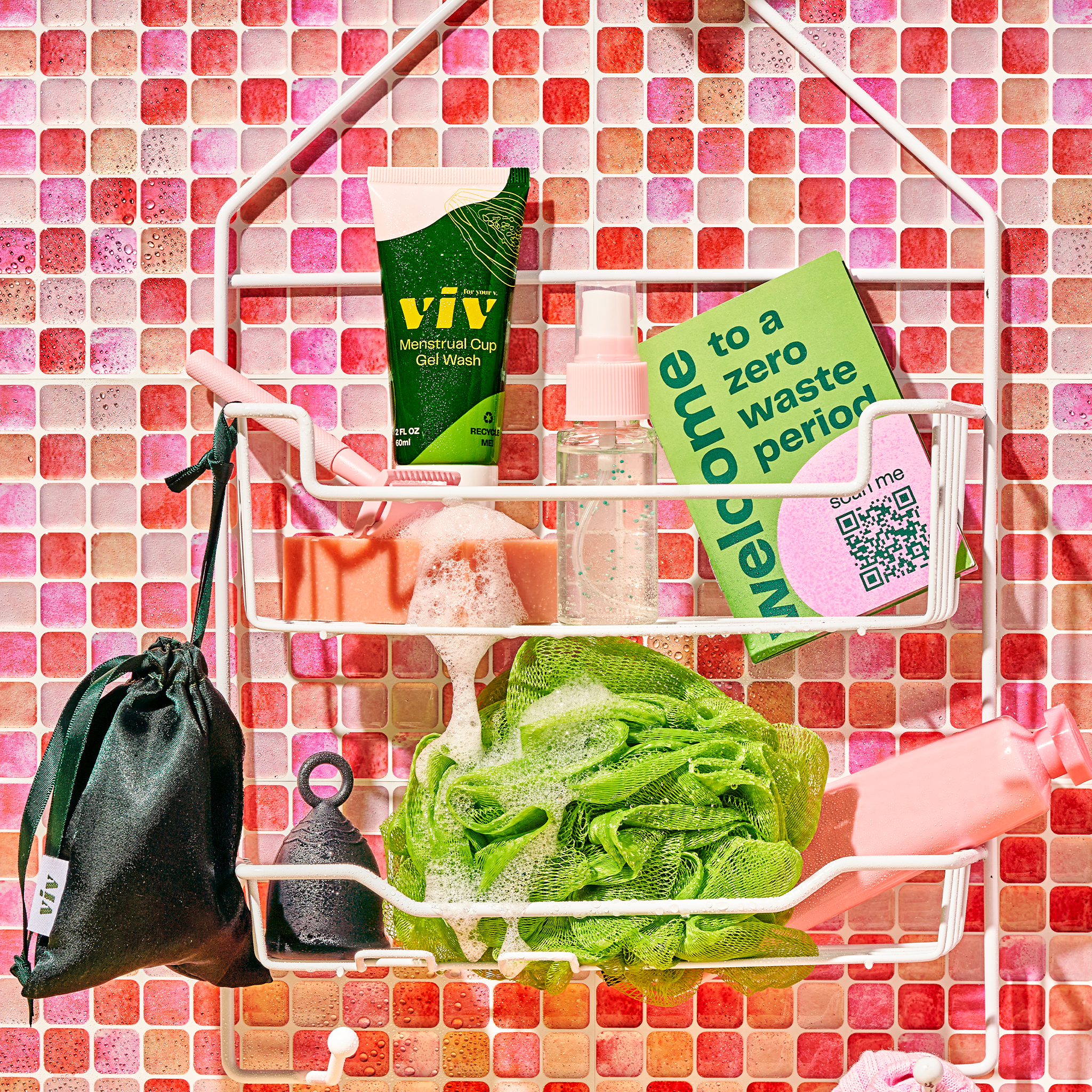 A white shelf hanging in a gen-z style pink tiled bathroom. On the shelf is various shower items, and the viv menstrual cup wash, beginner's guide, viv period cup, and the pouch.