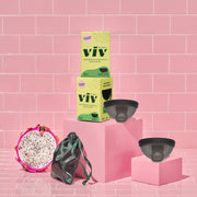Two Viv Menstrual Discs sit on top of a pink backdrop. The Viv Disc is a beginner-friendly menstrual disc, with a pull tab for easy disc removal. The Viv Disc is a dark color to prevent staining, and comes with a green silky storage pouch