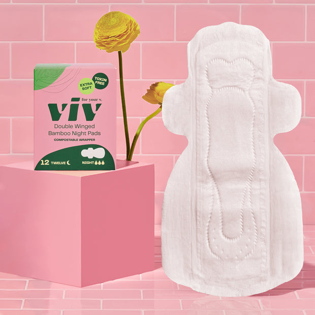 Viv Bamboo Double Winged Eco-Friendly Night Pads, extra long, ultra absorbent, chemical-free menstrual pads sit on a pink tile background with a box of Viv pads sitting next to it