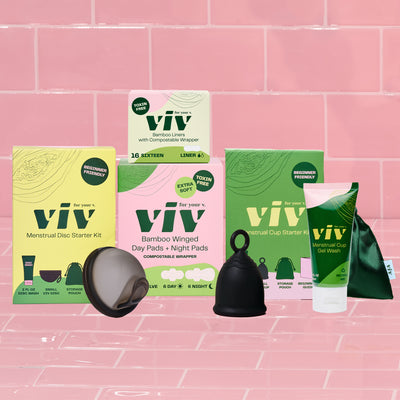 The Viv Menstrual Disc Starter Kit, Bamboo Liners, Bamboo Winged Pads, and Viv Menstrual Cup Starter Kit sit on a pink tile background, giving you the chance to try all period products in the Viv lineup for a more sustainable and toxin-free period.