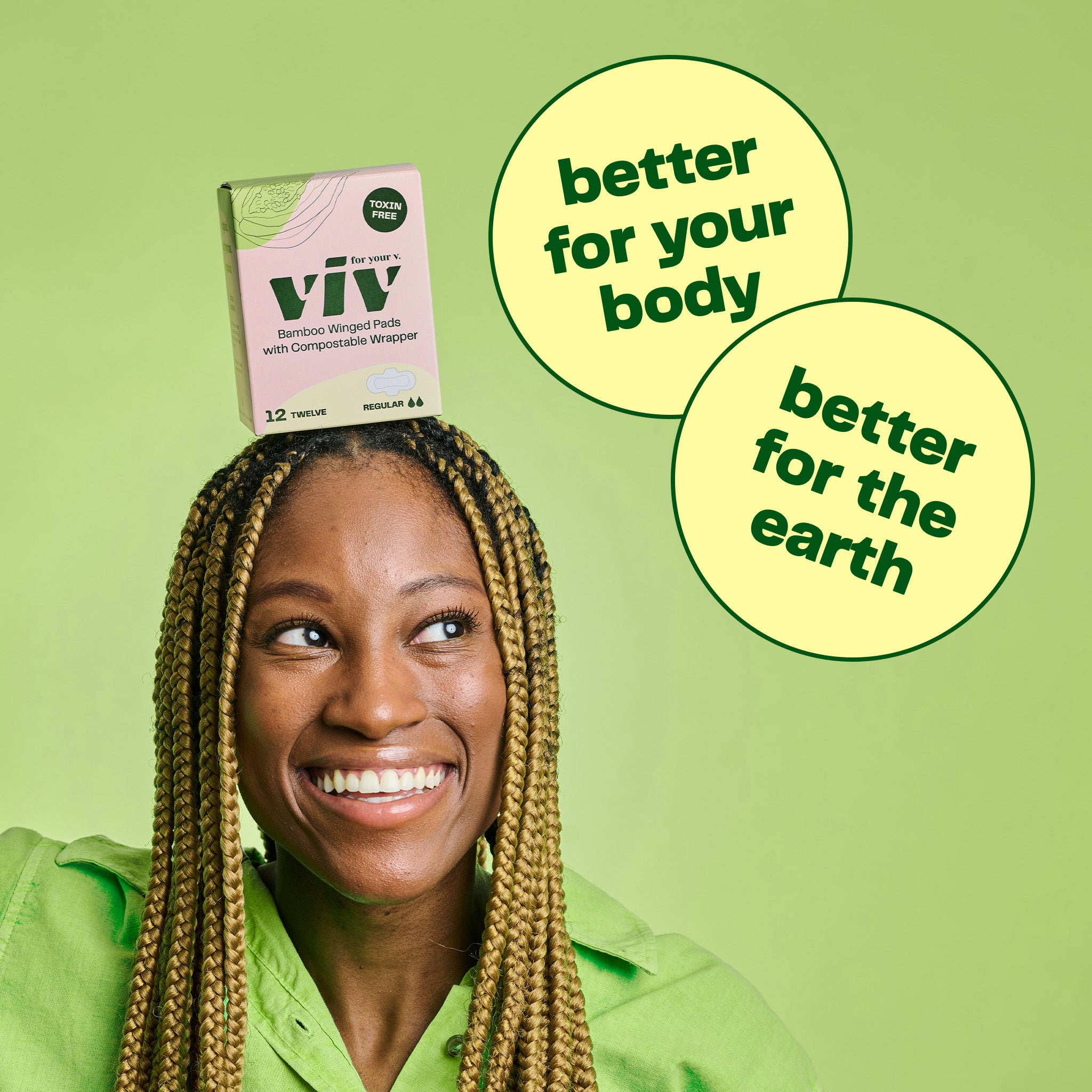 A box of Viv Winged Bamboo Pads sits on top of a smiling woman's head on a bright green background. Viv Pads are better for your body and better for the earth.