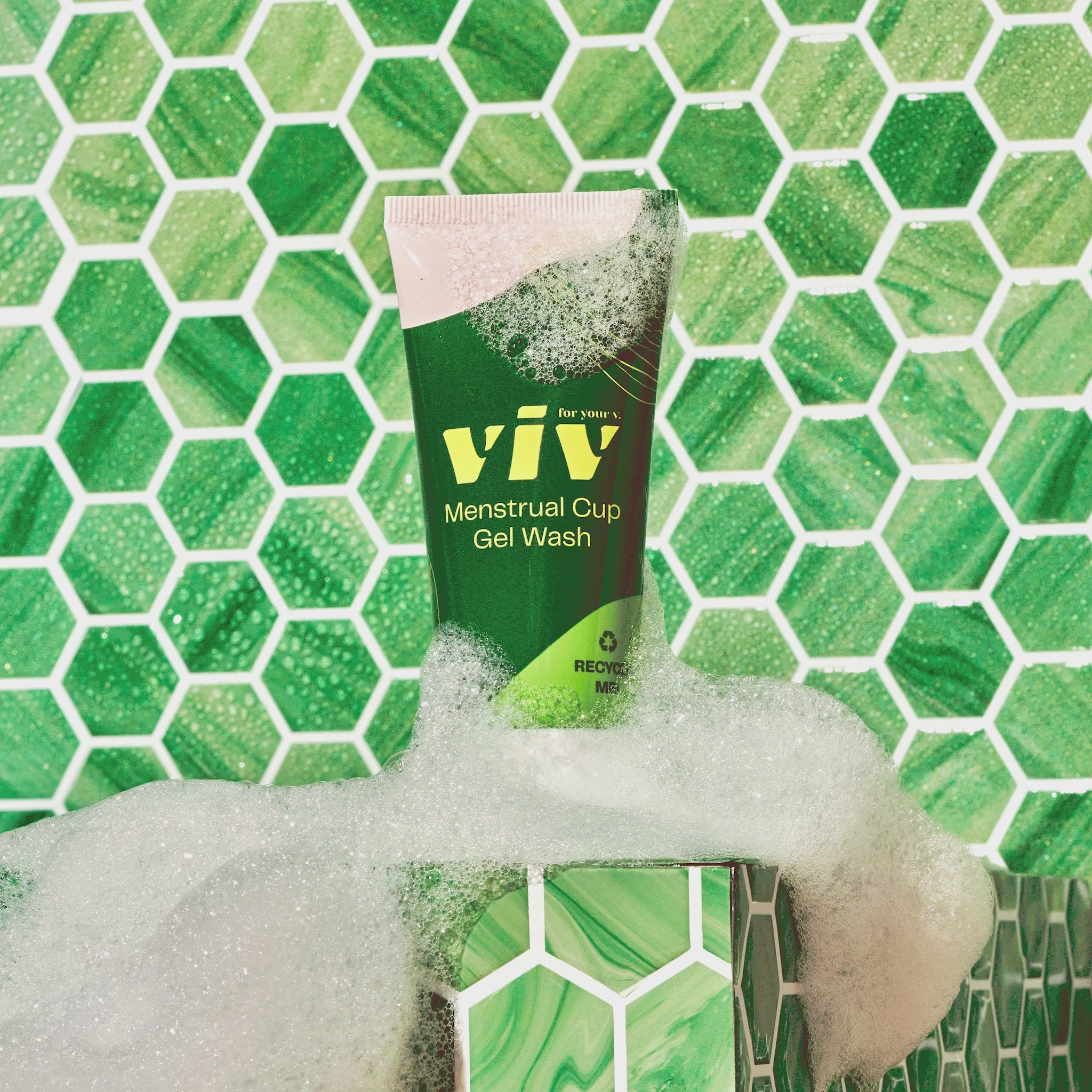 The all natural menstrual cup wash sits in a green tiled bathroom with foam around it